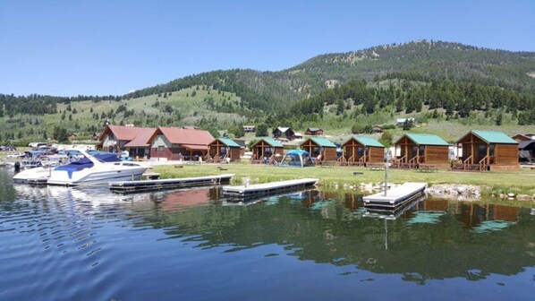 A lakeside lodge with multiple cabins, docked boats, and a mountainous backdrop.