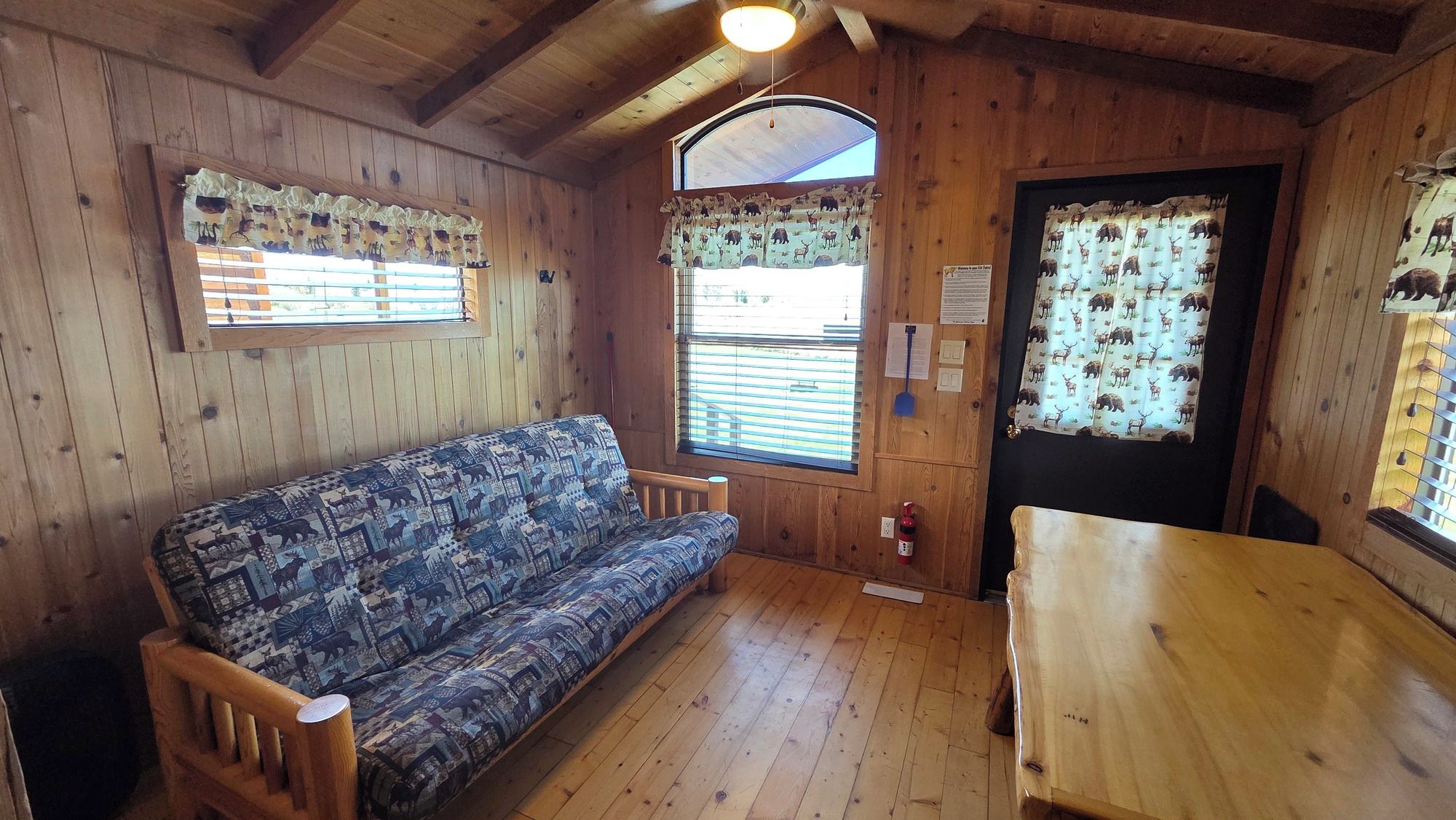Interior em madeira com sofá, mesa e janelas com cortinas estampadas.