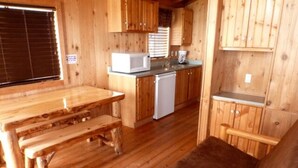 A wooden cabin interior with a kitchen area, a dining table, and a sofa. - Elk Haven Camping Cabin 11 (West Yellowstone)