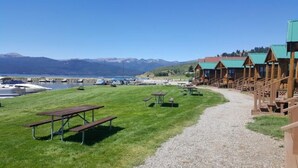 A lakeside lodge with wooden cabins, picnic tables, and a gravel path leading to the cabins. - Elk Haven Camping Cabin 11 (West Yellowstone)
