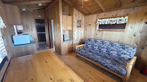 En inredning med träpanel, en soffa, ett litet bord, en liten köksdel och en dörr som leder till ett annat rum.