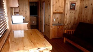 A wooden interior with a kitchen area, a dining table, and a sofa. - Elk Haven Camping Cabin 11 (West Yellowstone)