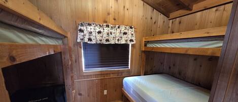 A bunk bed room with wooden walls and a window with blinds.