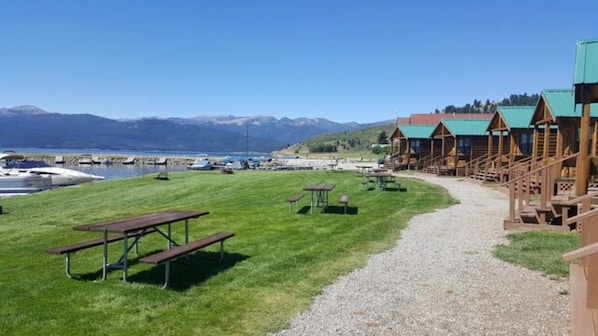 A lakeside lodge with wooden cabins, picnic tables, and a gravel path leading to the cabins.