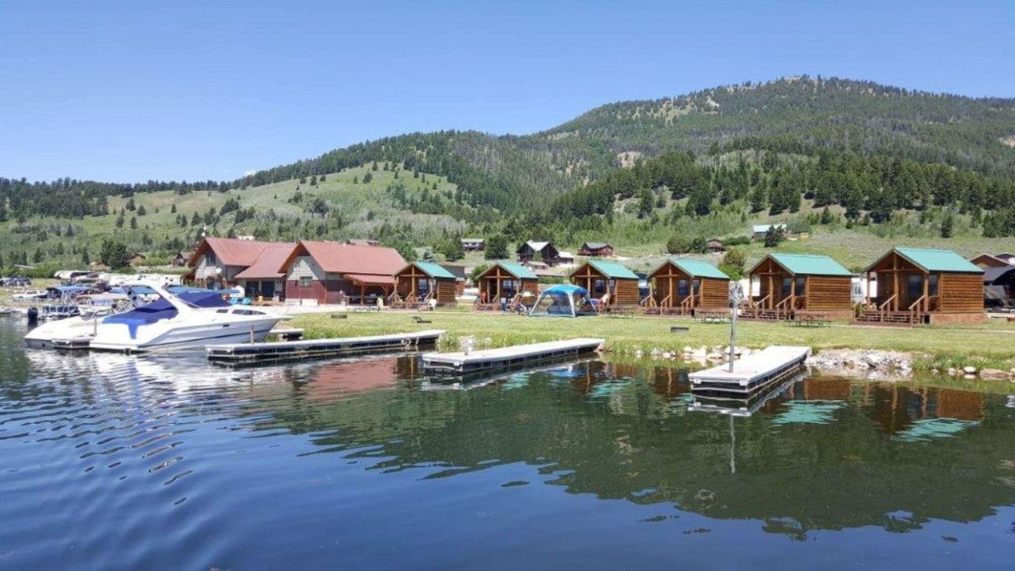 A lakeside lodge with multiple cabins, docked boats, and a mountainous backdrop.