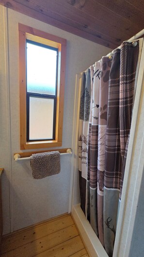 Et badeværelse med et vindue, et håndklædestativ og en bruseforhæng.