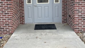 Puerta doble gris con paneles de vidrio y picaporte de metal, ubicada en una pared de ladrillo con felpudo de hormigón.