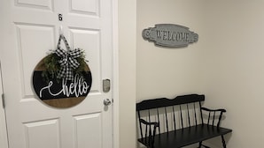 Una puerta blanca con un letrero que dice 'hello' y otro que dice 'welcome' sobre un banco negro.