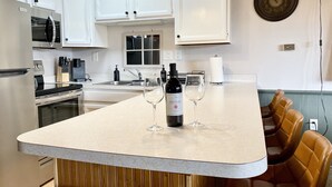 Une cuisine avec des meubles blancs, un réfrigérateur en acier inoxydable, un four à micro-ondes, un évier et une bouteille de vin posée sur le comptoir.