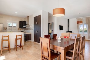 A modern kitchen with a dining area, wooden chairs, a table, and a hanging light fixture.