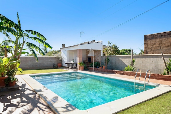 A swimming pool with a patio area, a small building, and potted plants.