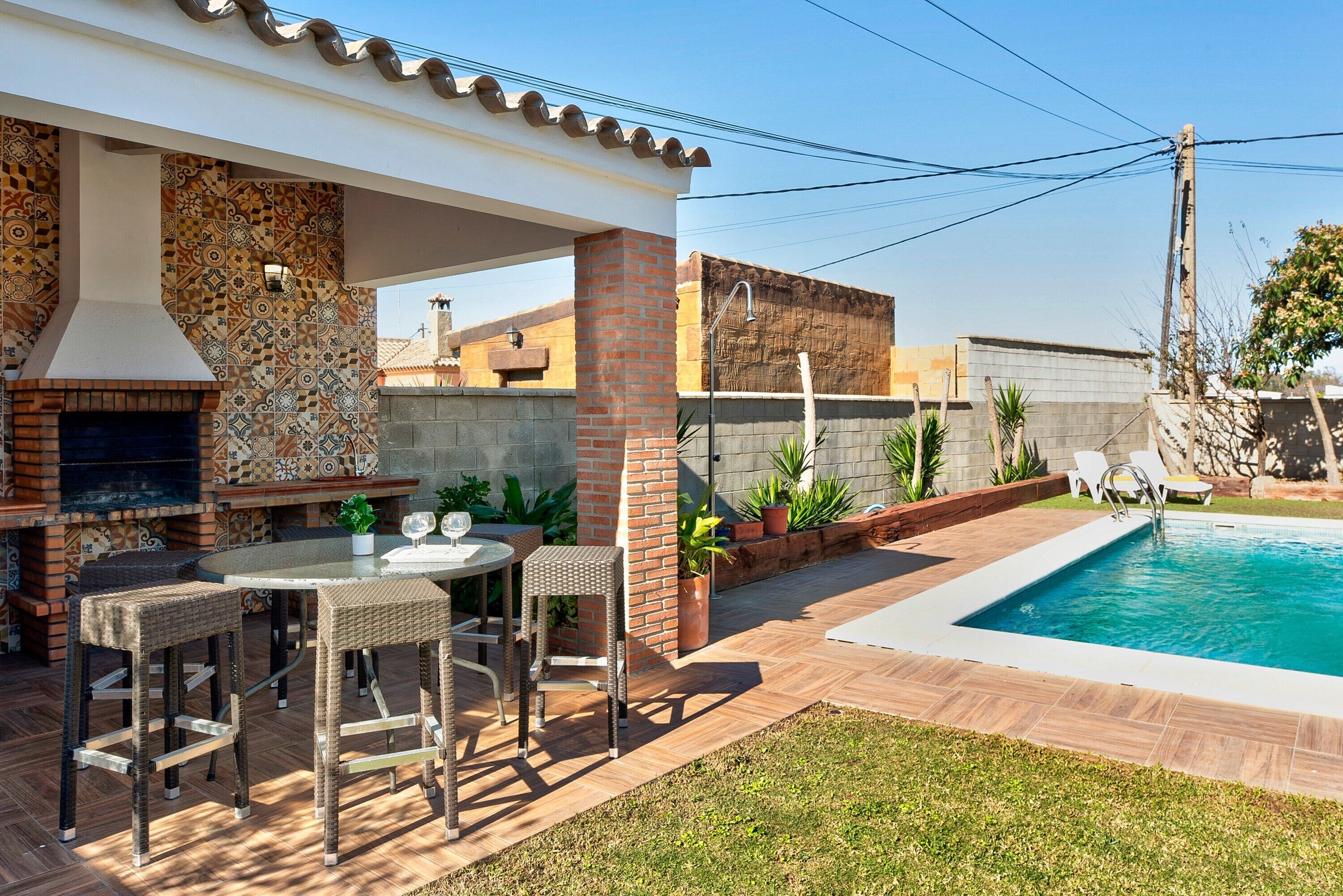 Une terrasse extérieure dotée d’une cheminée en briques, d’une piscine et d’un coin repas avec des meubles en osier.