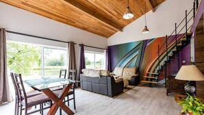 Ein modernes Wohnzimmer mit einem Glastisch, Sofas, einer Treppe und Blick ins Grüne.