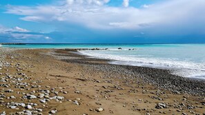 A beach with pebbles and sand, a clear sky, and calm sea.