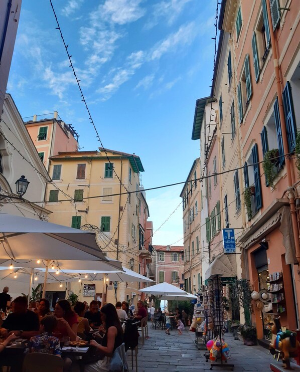 A narrow street with buildings on either side, outdoor seating, and a blue sign indicating a tobacconist.