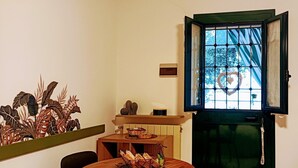 Ein Essbereich mit einem runden Holztisch, Stühlen, einer kleinen Ablage mit Dekoration, einem Fenster mit Blick auf Bäume und einer grünen Tür.