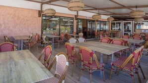 An indoor dining area with wooden tables and wicker chairs, large windows, and a high ceiling. - Mobile Home 'Mobilhome Oasis Village Puget Argen' with Shared Pool and Private Terrace (Puget-sur-Argens)