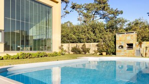 Una casa moderna con piscina, ventanas amplias y un muro de piedra con una parrilla.