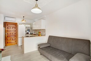 A modern kitchen with a built-in oven, a wooden door, and a grey sofa in the living area.