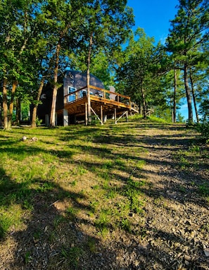 A house with a wooden deck, surrounded by trees and a grassy area.