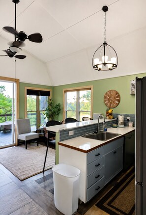 A kitchen with a central island, a dining area with chairs, a ceiling fan, and a clock on the wall.