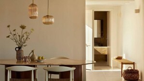 Un coin repas avec une table ronde, deux chaises, des lampes suspendues et un vase rempli de fleurs.