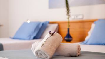 A neatly made bed with two rolled towels and a vase with a plant.