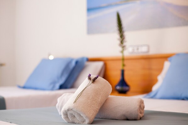 A neatly made bed with two rolled towels and a vase with a plant.