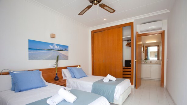Habitación de hotel con dos camas, un ventilador de techo, un cuadro de playa y un armario de madera.