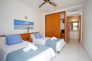 Ein Hotelzimmer mit zwei Betten, einem Deckenventilator, einem Strandbild und einem Holzschrank.