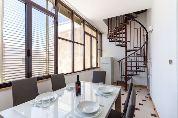 A dining area with a table set for two, a bottle of wine, and a spiral staircase in the background.