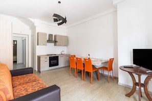 A modern kitchen with white cabinets, a dining table with orange chairs, a TV on a wooden stand, and a patterned orange sofa. - Holiday Home 'A Pochi Passi Dalla Spiaggia' with Air Conditioning (Ugento)