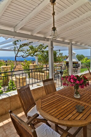 A covered outdoor patio with a wooden table and chairs, a hanging light fixture, and a view of the ocean. - Holiday Home 'Villa Ntora' with Mountain View, Wi-Fi and Air Conditioning (Afiartis)
