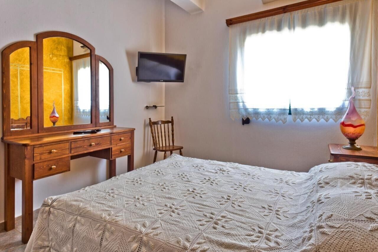 Ein Schlafzimmer mit einem Bett, einem Holzschrank mit Spiegel, einem Fernseher und einem Fenster mit Vorhängen.