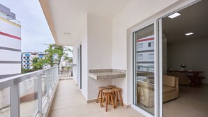 A balcony with a glass door, a small bar area with stools, and a view of the street and buildings. - Beach Praia Grande Ubatuba (Ubatuba)