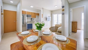 A modern kitchen with stainless steel appliances, a dining area with a wooden table set for four, and a view into the living room. - Beach Praia Grande Ubatuba (Ubatuba)