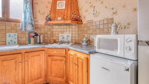 Una cocina con armarios de madera, un microondas, un refrigerador, un lavaplatos y una ventana con cortina.