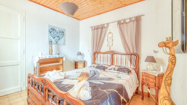 Un dormitorio con techo de madera, una cama con colcha estampada, una mesita de noche con lámpara y un atrapasueños colgado en la pared.