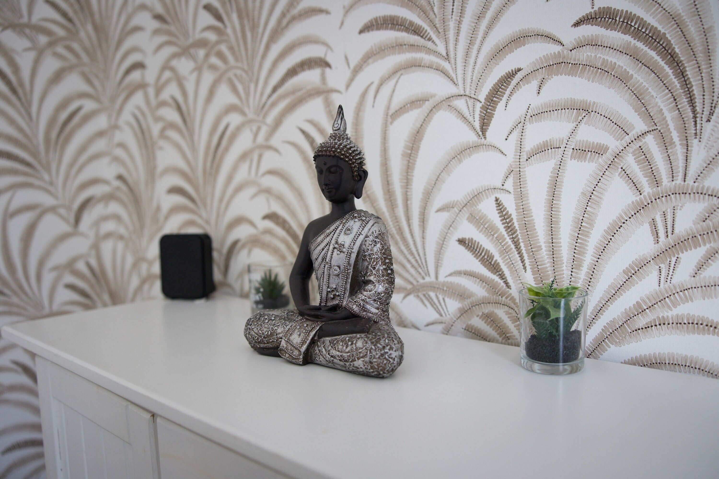 A statue of a seated figure on a white surface, a small potted plant, and a patterned wallpaper.