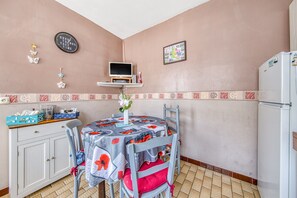 Eine Küche mit Esstisch, Stühlen, einem Kühlschrank, einer Uhr und einem kleinen Fernseher auf einem Regal.
