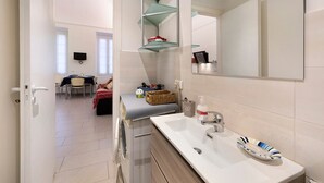 A modern bathroom with a large mirror, a white sink, and a glass shelf unit. - Apartment 'Smart Home Loano' with Wi-Fi and Air Conditioning (Loano)
