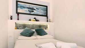 A hotel room with a bed, pillows, a headboard, a flat-screen TV, and a wall-mounted shelf with various items. - Apartment 'Smart Home Loano' with Wi-Fi and Air Conditioning (Loano)