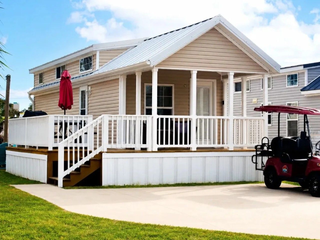 Une maison à deux étages avec un porche abrité, un chariot de golf rouge et une pelouse bien entretenue.