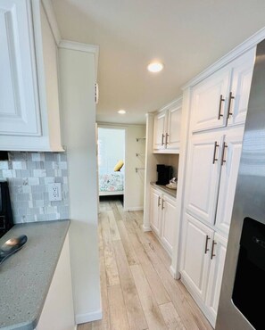 A kitchen with white cabinets, a countertop, and a wooden floor. - Vacation Cottage North Myrtle Beach #69 (North Myrtle Beach)