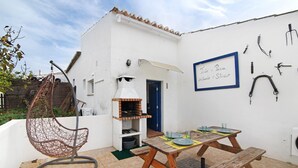 Un patio con una silla colgante, una mesa de madera y una parrilla.