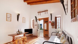 Una habitación con una mesa de madera, asientos tipo banco, una cama con estructura metálica y un televisor.
