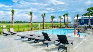 A pool area with lounge chairs and palm trees, surrounded by a fenced field. - Vacation Cottage North Myrtle Beach #65 (North Myrtle Beach)
