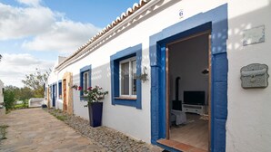 Een wit gebouw met blauwe details, een stenen pad en een deur die leidt naar een kamer met een televisie.