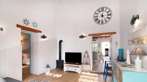 Een woonkamer met een televisie, houten vloeren, een klok en een trap naar een andere kamer.