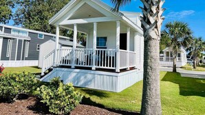 A single-story house with a porch, surrounded by well-maintained lawns and palm trees. - Vacation Cottage North Myrtle Beach #67 (North Myrtle Beach)